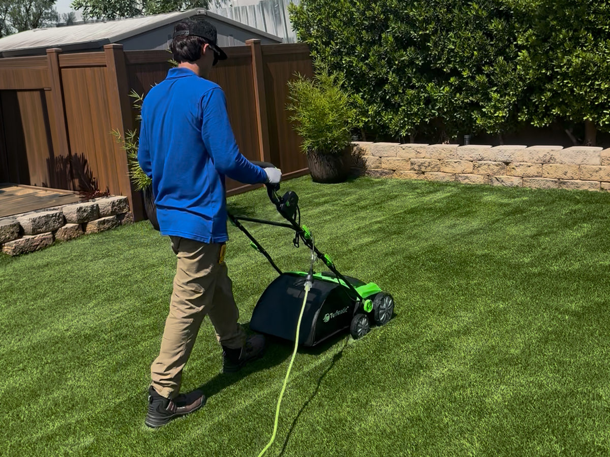 The Doggo Scoop technician grooming artificial turf with a power rake